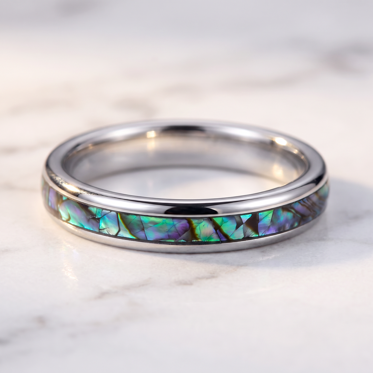 The Iris silver color tungsten ring with an abalone shell inlay lying flat on a marble surface