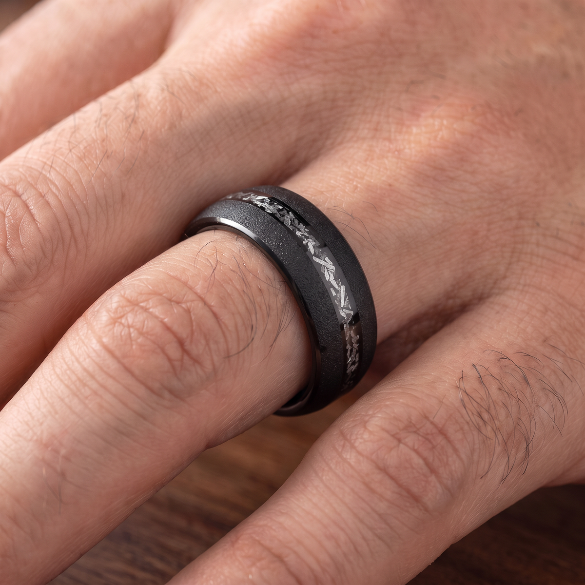 Close up of a man's hand wearing The Stardust black sandblasted tungsten ring with meteorite inlay