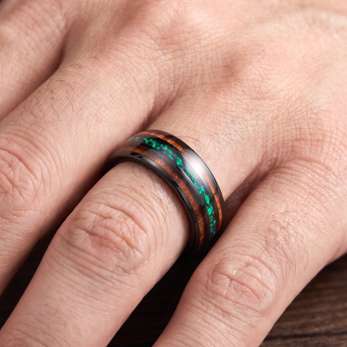 Close up of a man's hand wearing The Canopy black tungsten ring with green opal and koa wood inlays