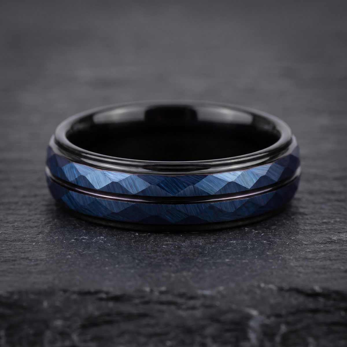 The Lattice black tungsten ring with a blue rhombus cut face lying flat on a dark slate surface