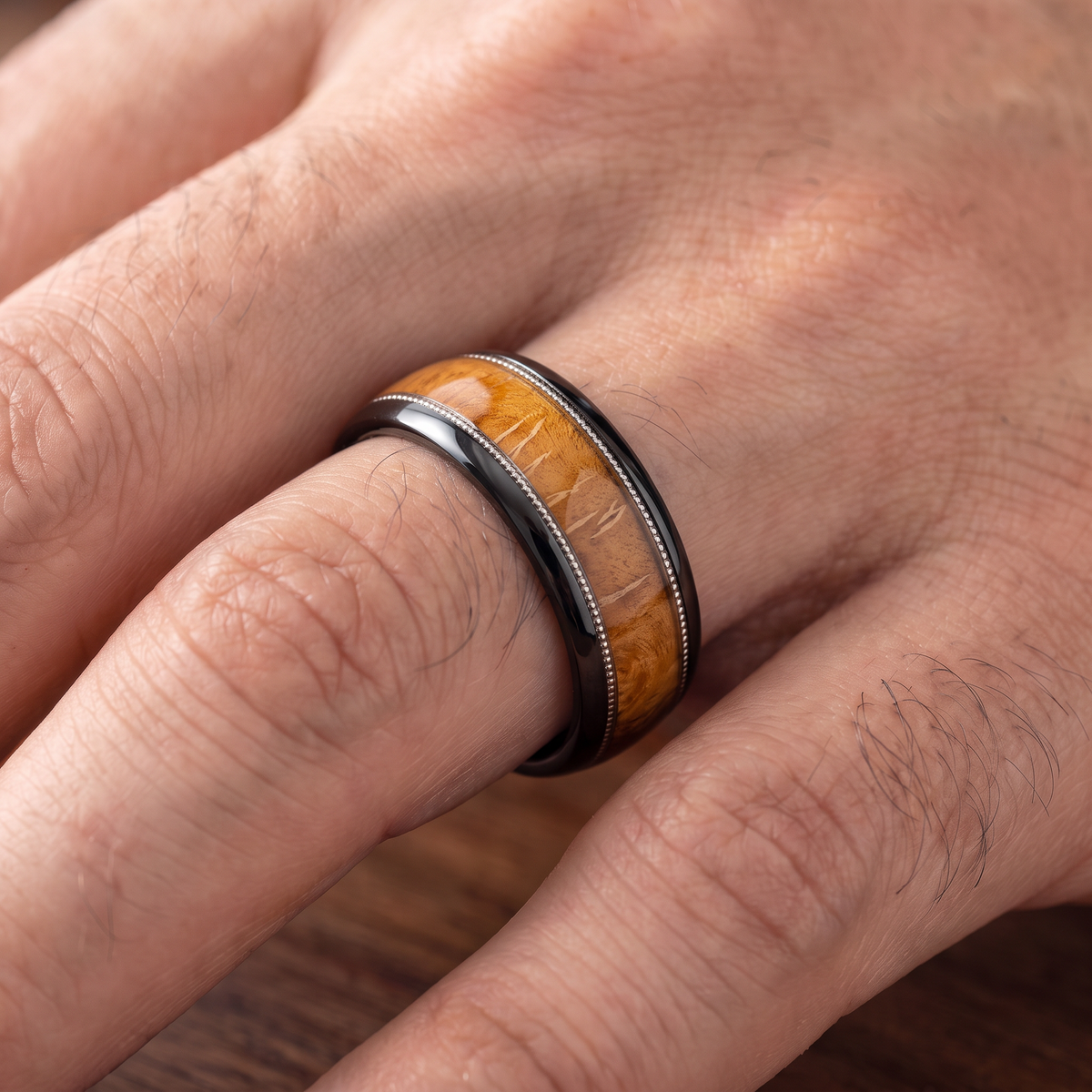 Close up of a man's hand wearing The Encore black tungsten ring with whiskey barrel wood inlay