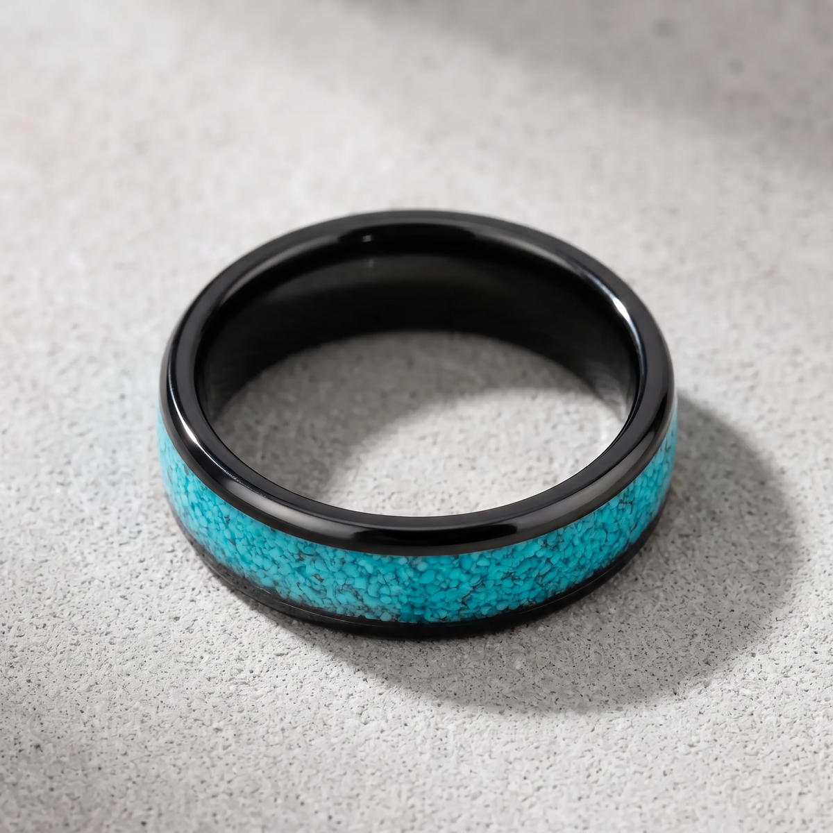 The Lagoon black tungsten ring with turquoise inlay lying flat on a light grey surface