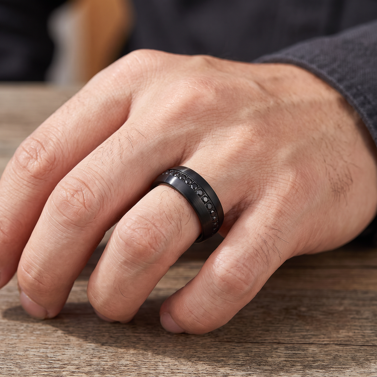 Close up of a man's hand wearing The Obsidian black brushed tungsten ring with black CZ stones