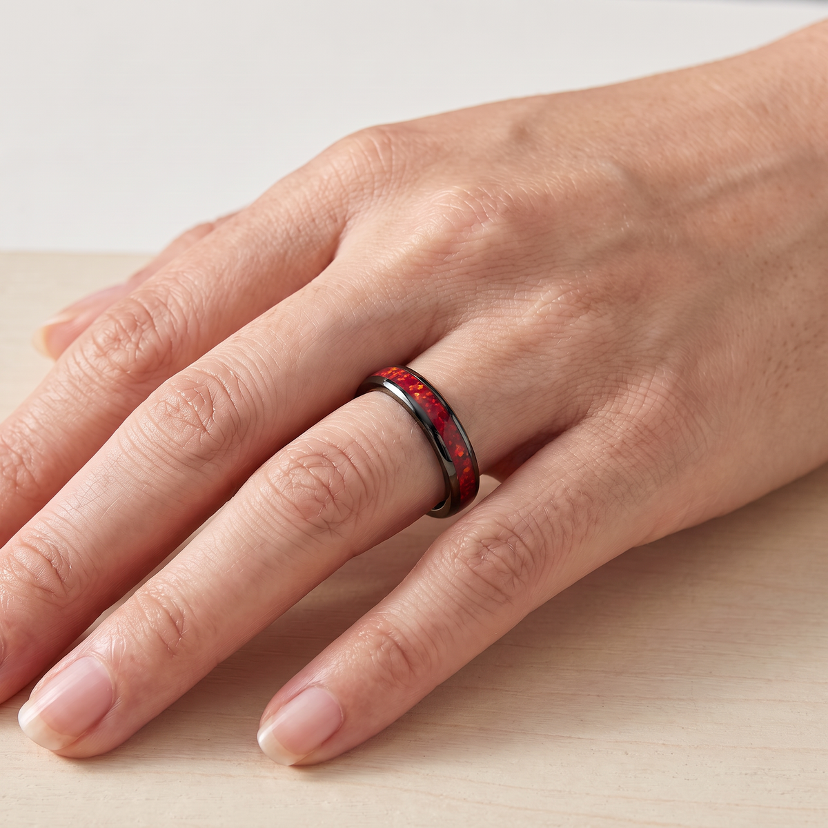 Close up of a woman's hand wearing The Cinder black tungsten ring with a red opal inlay