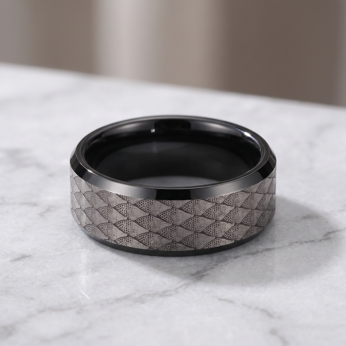 The Serpentine tungsten ring with a black interior lying flat on a light grey marble surface