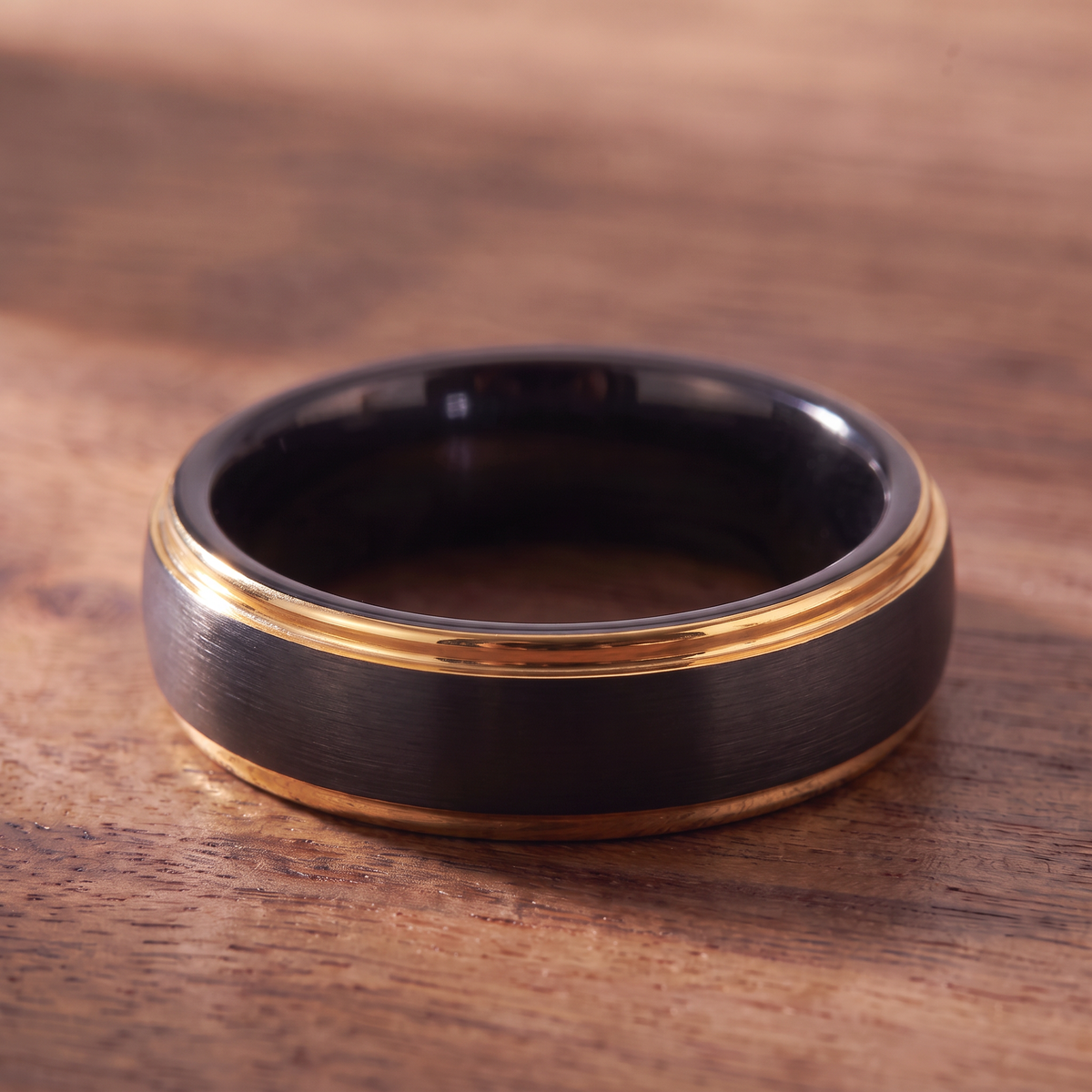 The Corona black tungsten ring lying flat on dark walnut wood