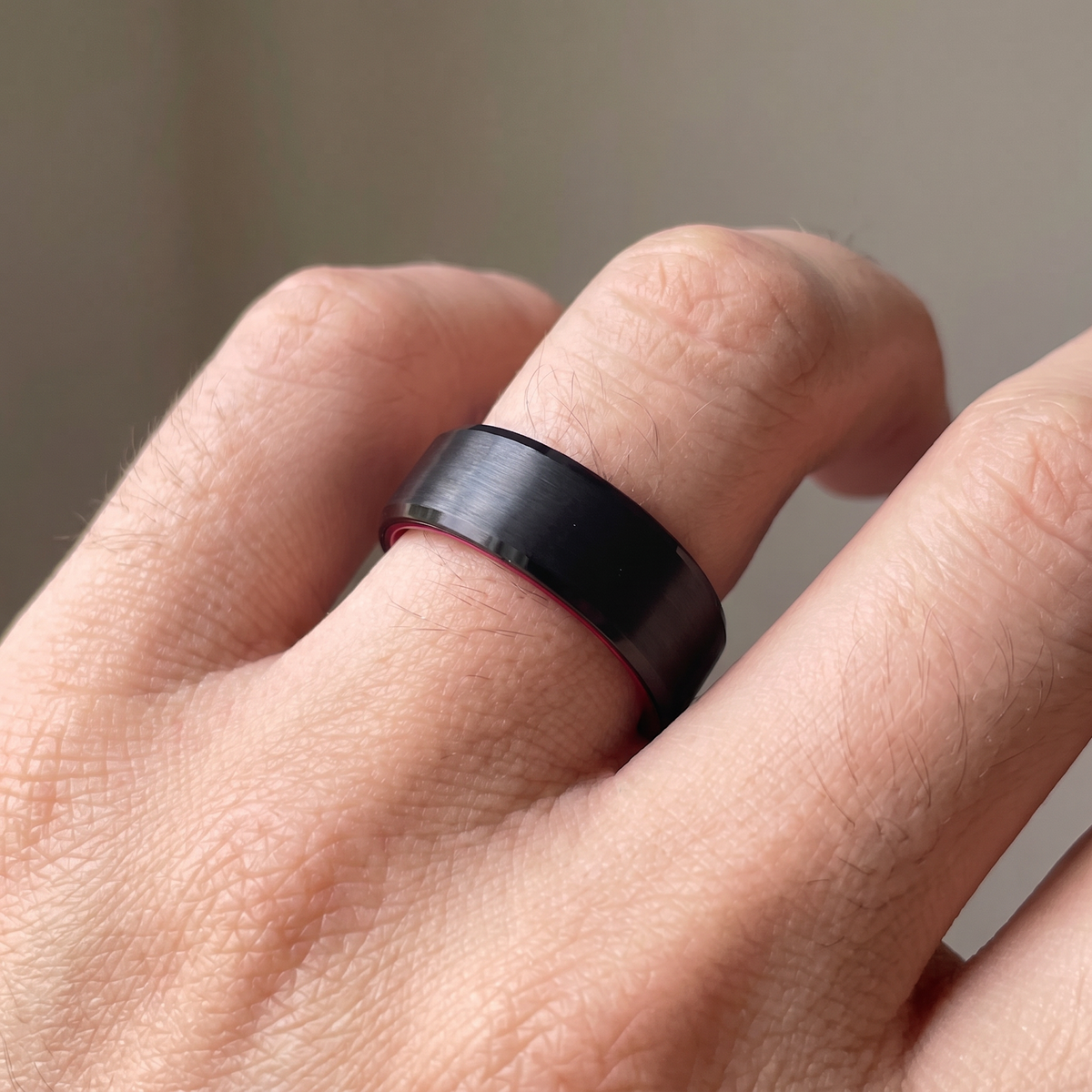 Close-up of a man's hand wearing The Redline black brushed tungsten ring