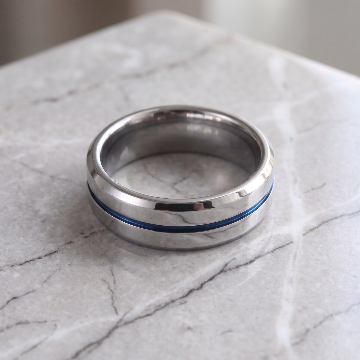 The Meridian tungsten ring with a blue groove line lying flat on a light grey marble surface