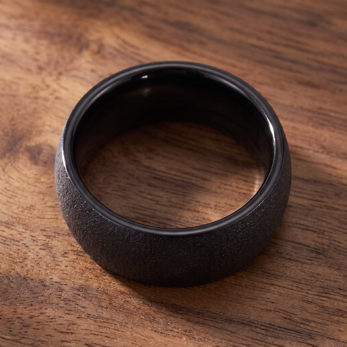 The Basalt black sandblasted tungsten ring lying flat on a walnut wood surface