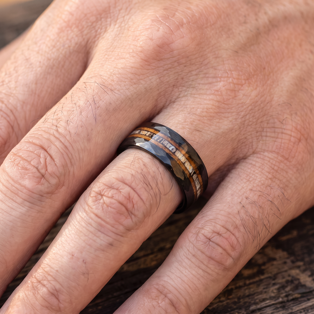 Close up of a man's hand wearing The Cooper tungsten ring with whiskey barrel wood and deer antler inlay