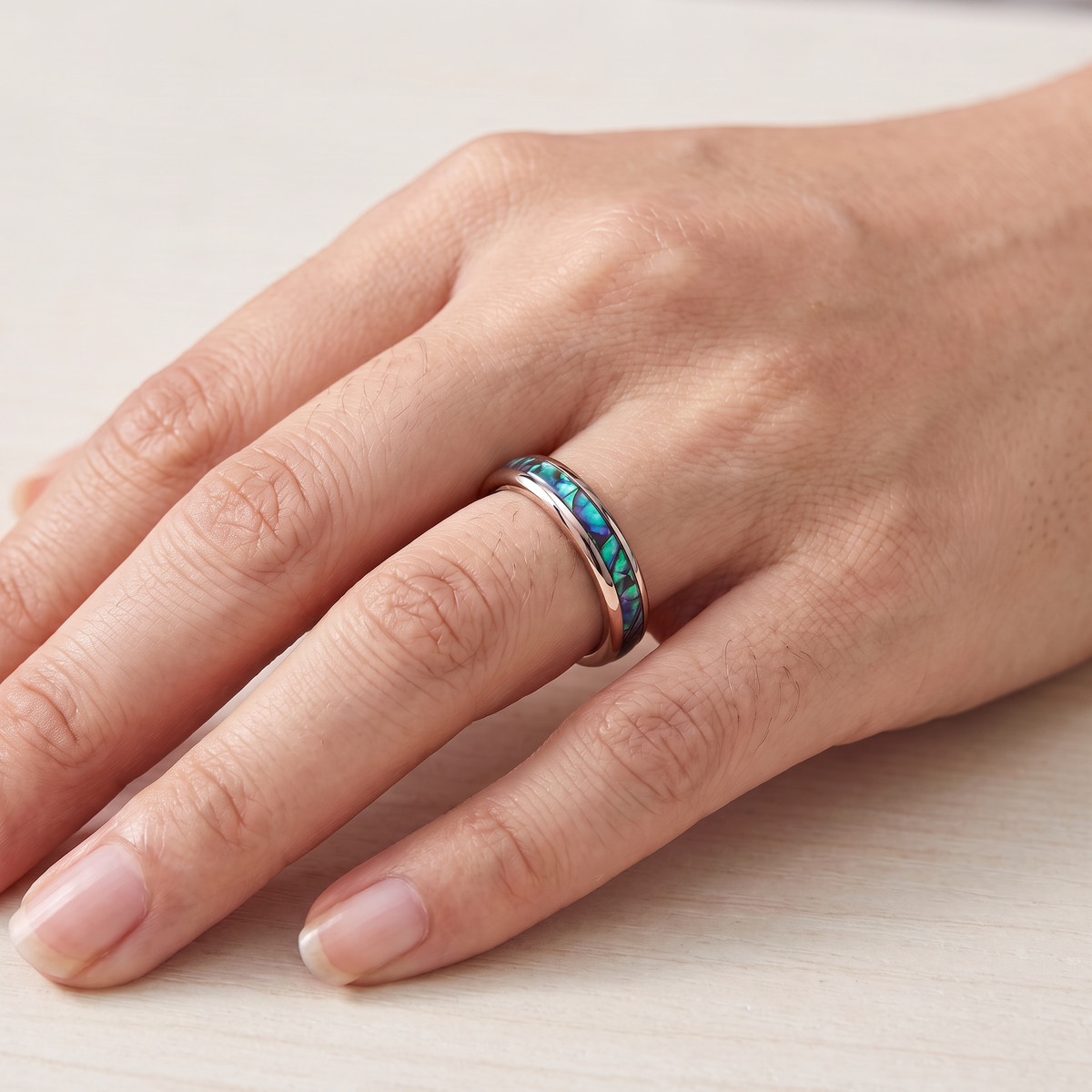 Close up of a woman's hand wearing The Iris rose color tungsten ring with an abalone shell inlay