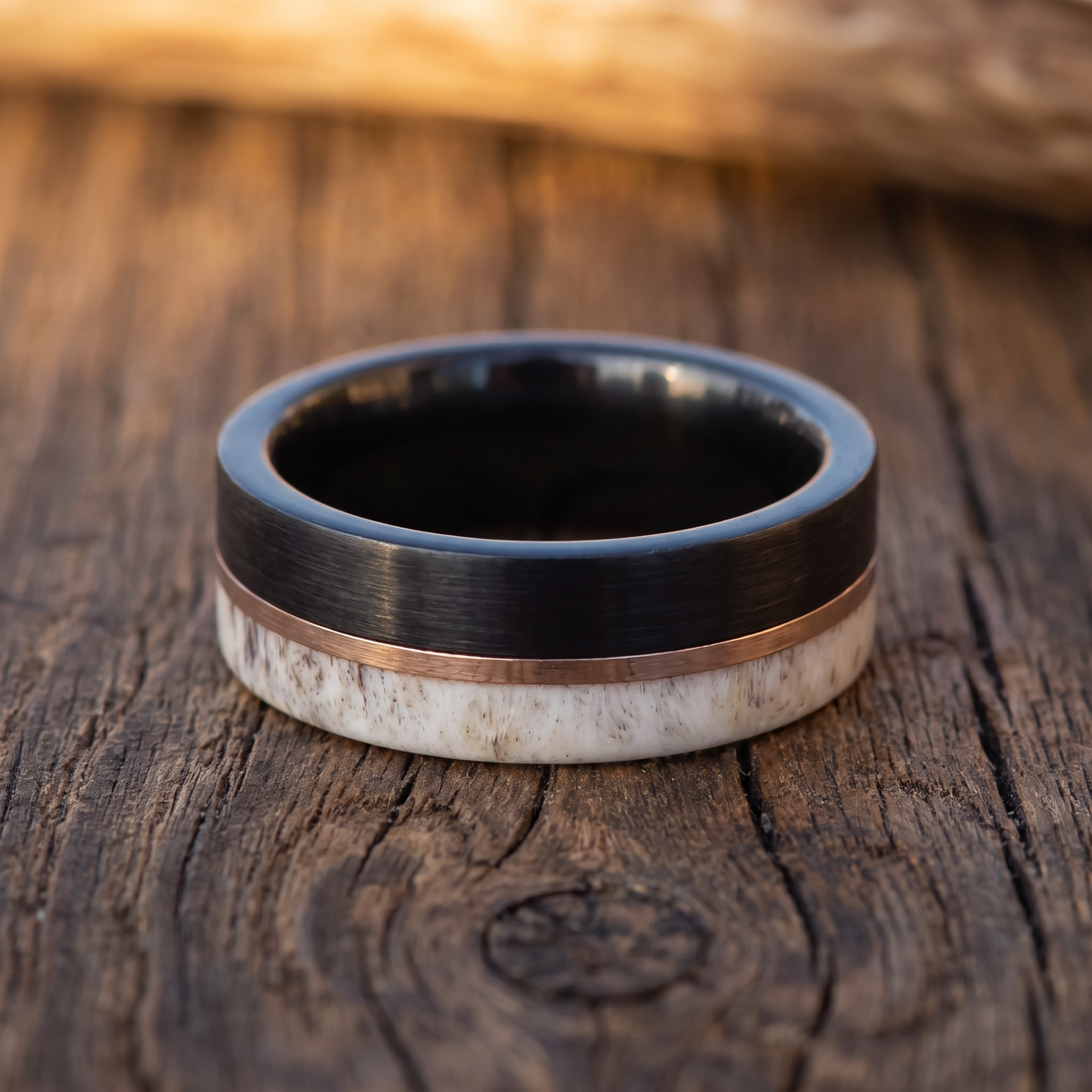 The Stag tungsten ring with a deer antler inlay lying flat on a weathered dark oak surface