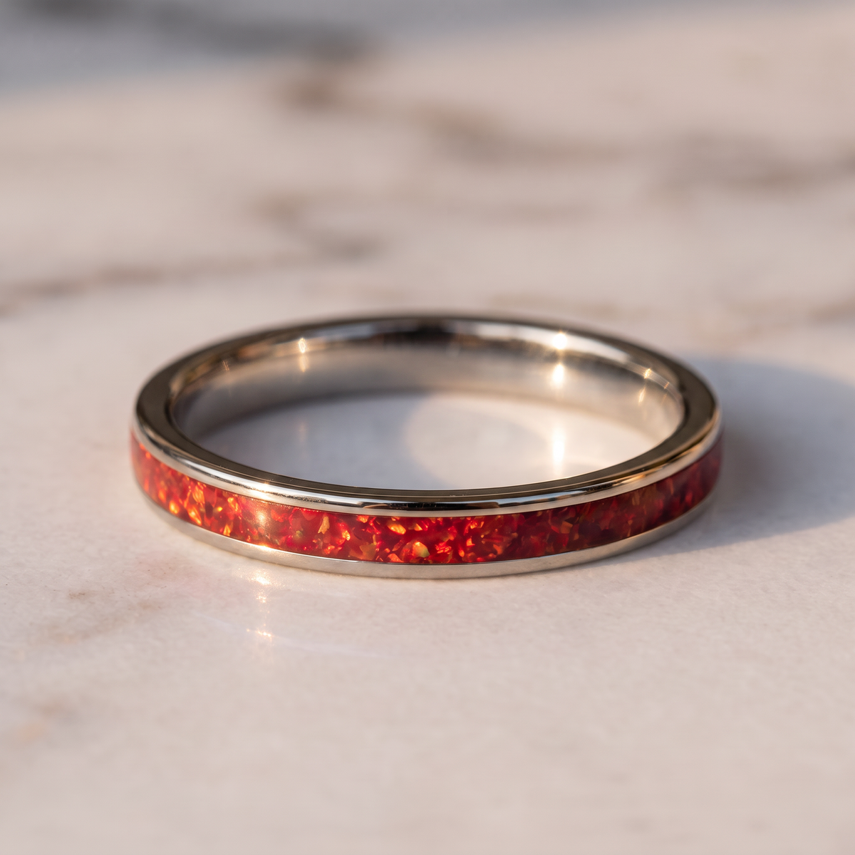 The Cinder silver color tungsten ring with a red opal inlay lying flat on a marble surface