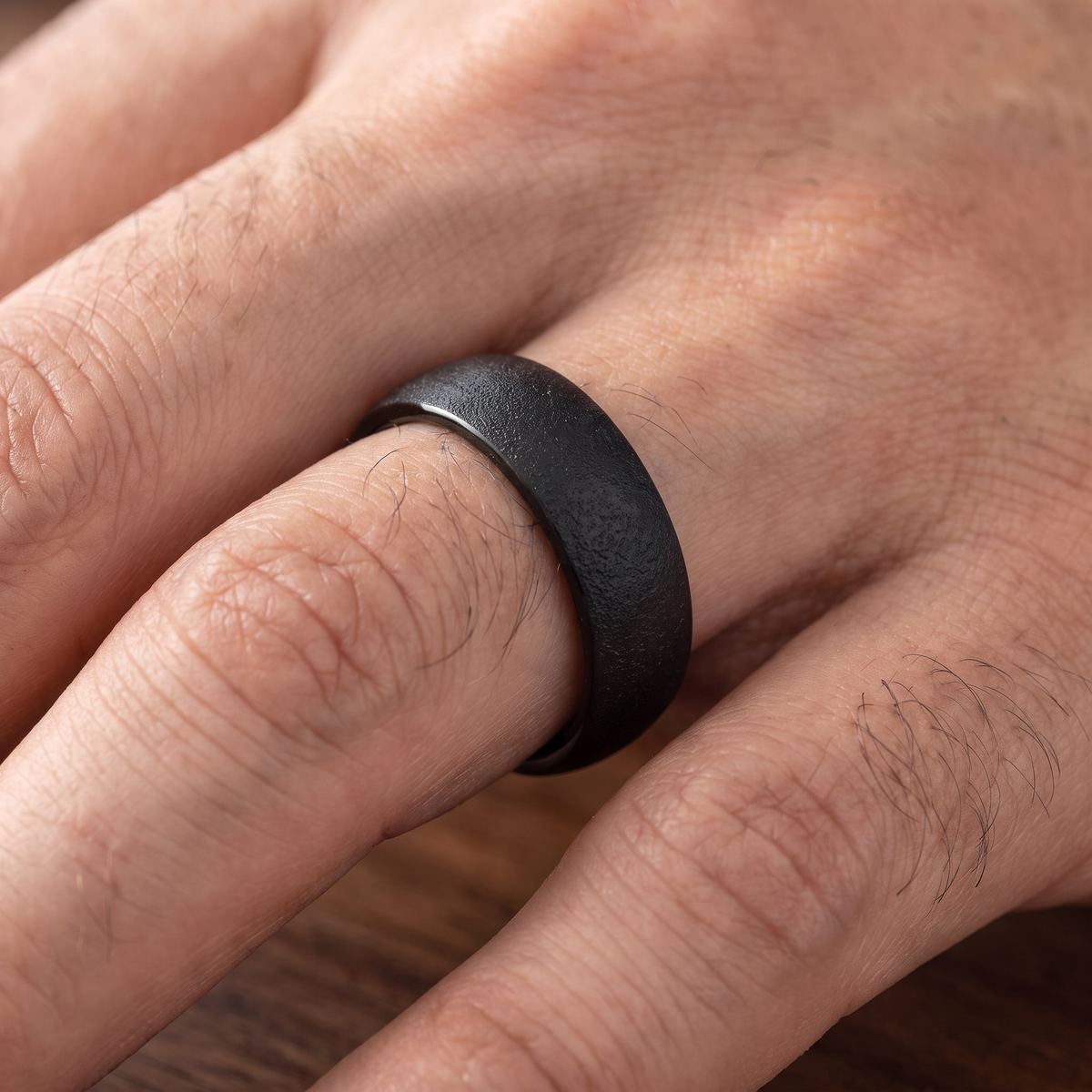 Close up of a man's hand wearing The Basalt black sandblasted tungsten ring