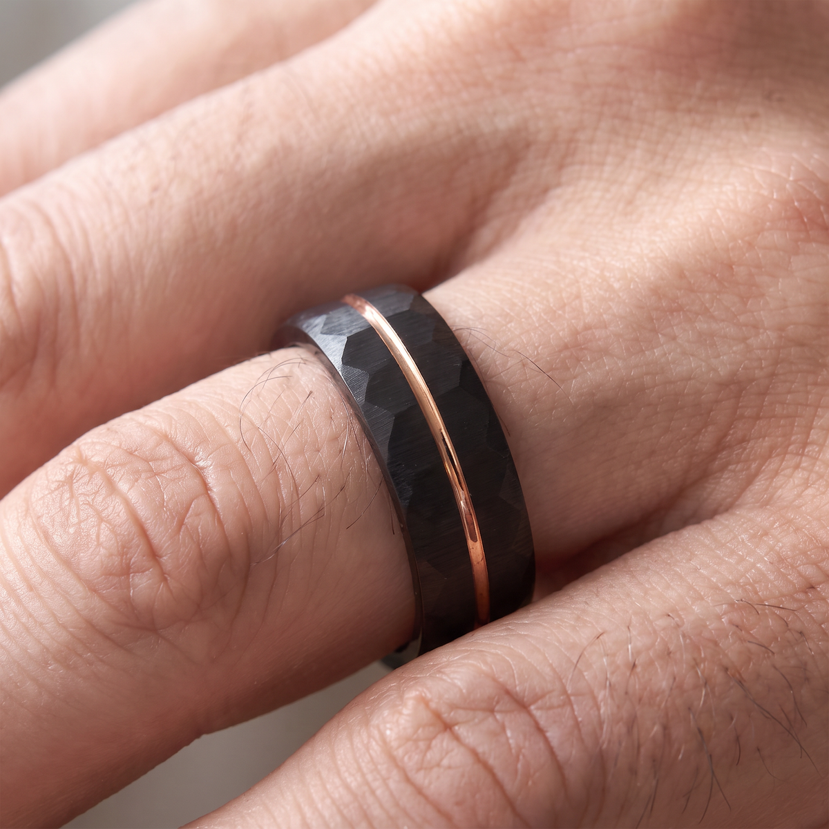 Close-up of a man's hand wearing The Daybreak black hammered tungsten ring with rose gold groove