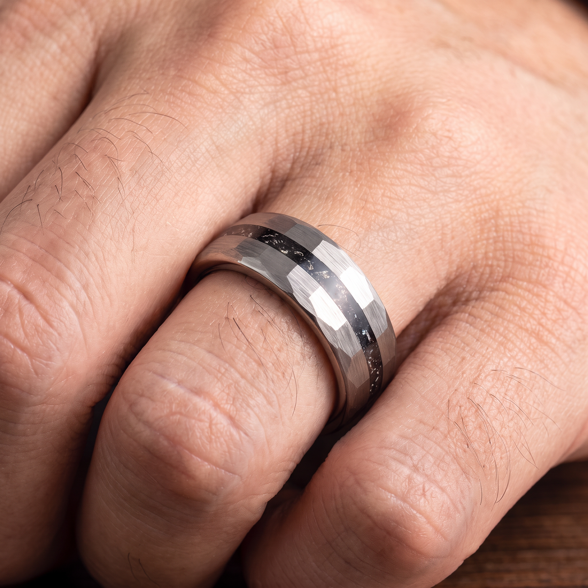 Close up of a man's hand wearing The Meteor hammered tungsten ring with a meteorite fragment inlay