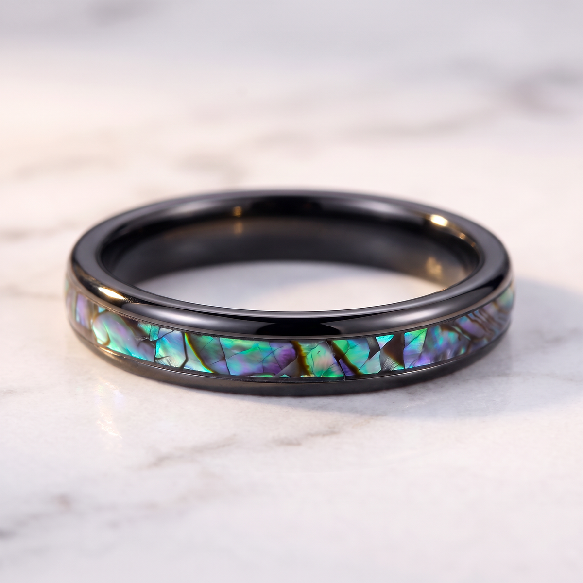 The Iris black tungsten ring with an abalone shell inlay lying flat on a marble surface