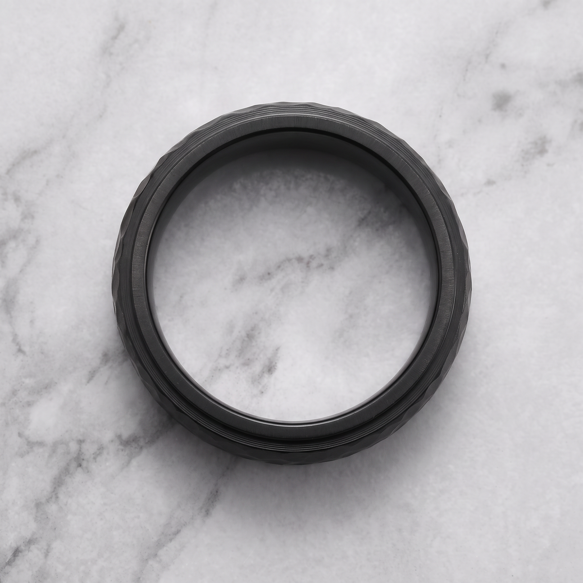 The Crater black hammered ring lying flat on a light grey marble surface
