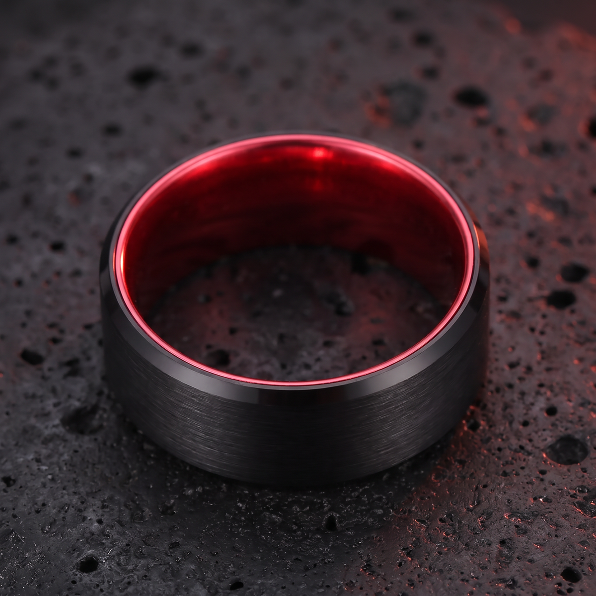 The Redline tungsten ring lying flat on black volcanic stone showing the red interior