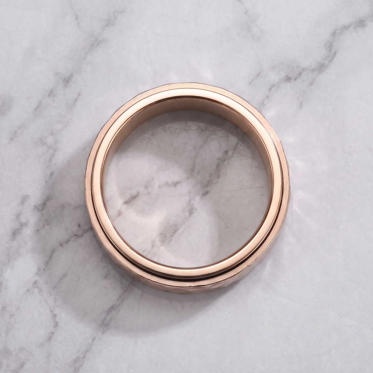 The Orbit rose spinner ring lying flat on a light grey marble surface