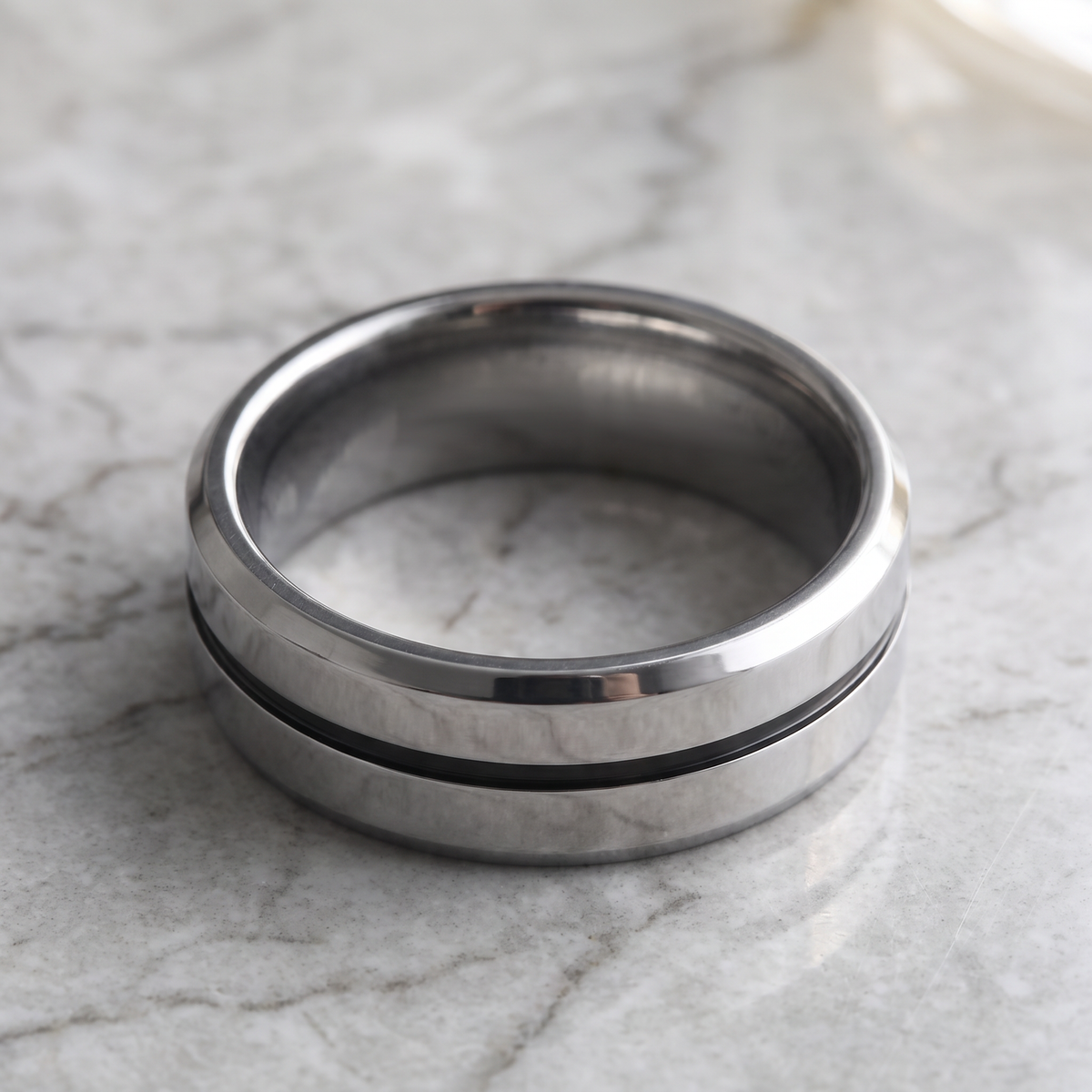 The Meridian tungsten ring with a gray groove line lying flat on a light grey marble surface
