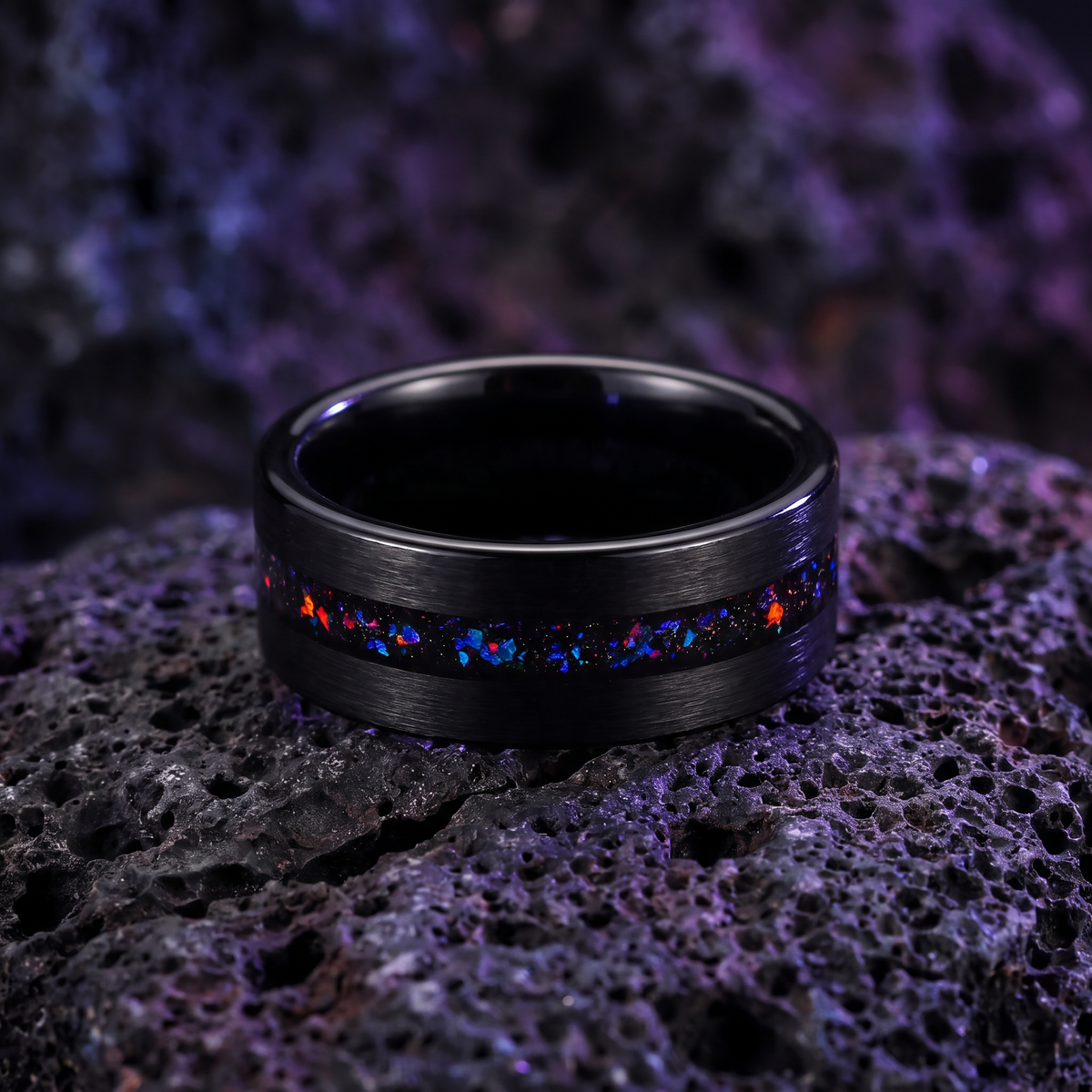 Black sandblasted tungsten ring with opal inlay lying flat on dark volcanic stone