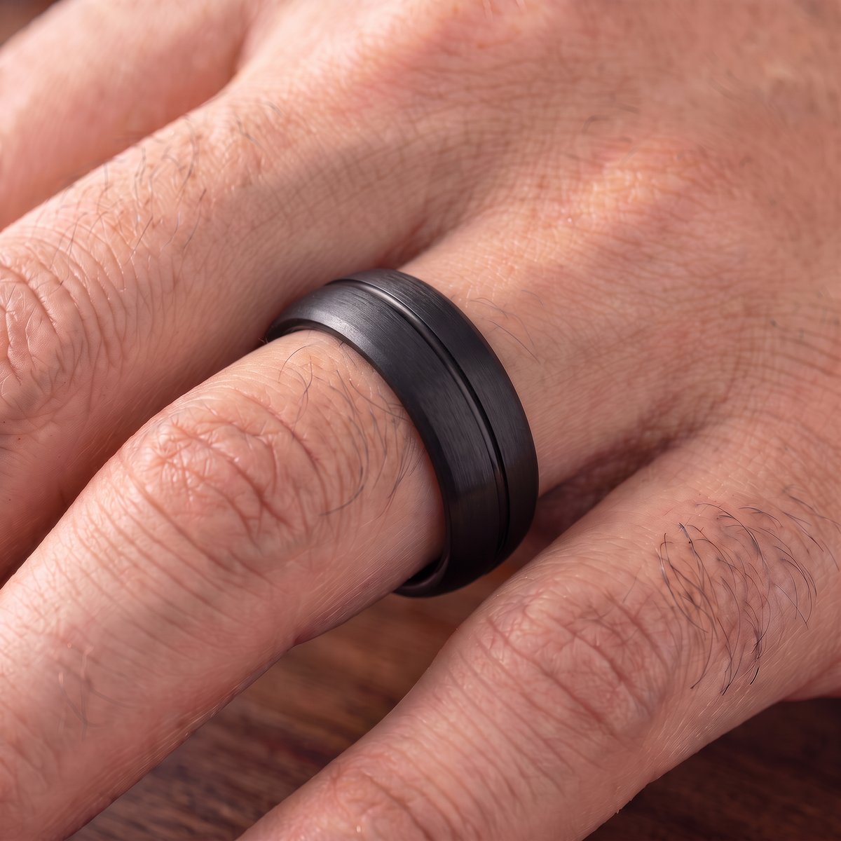 Close up of a man's hand wearing The Furrow black brushed tungsten ring with a groove