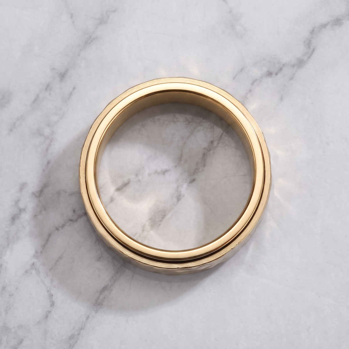 The Orbit gold spinner ring lying flat on a light grey marble surface