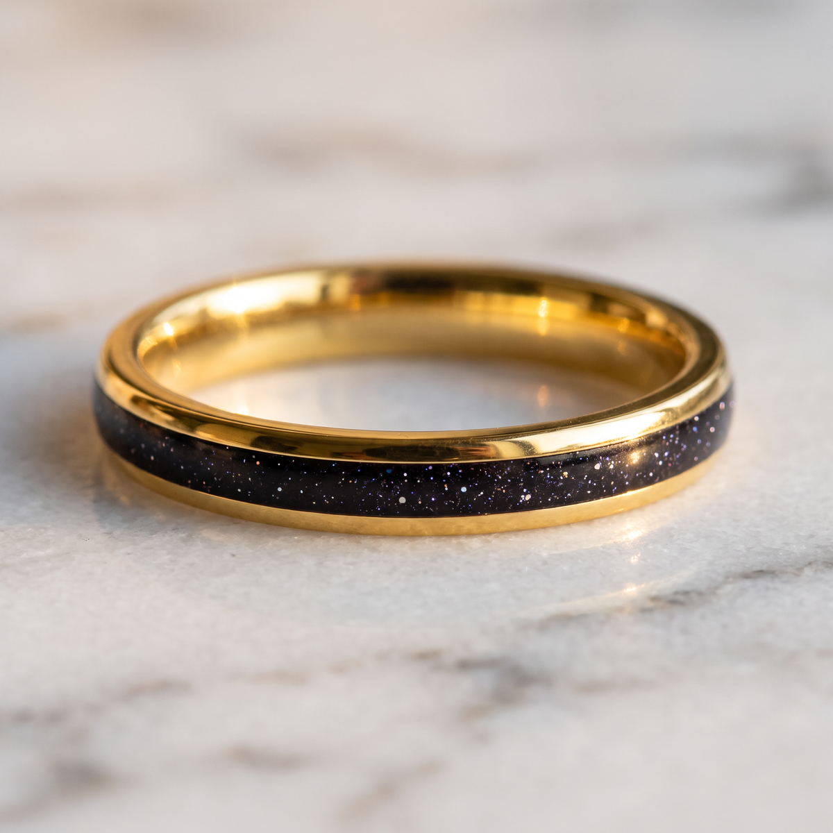 The Vega gold color tungsten ring with a galaxy opal inlay lying flat on a marble surface