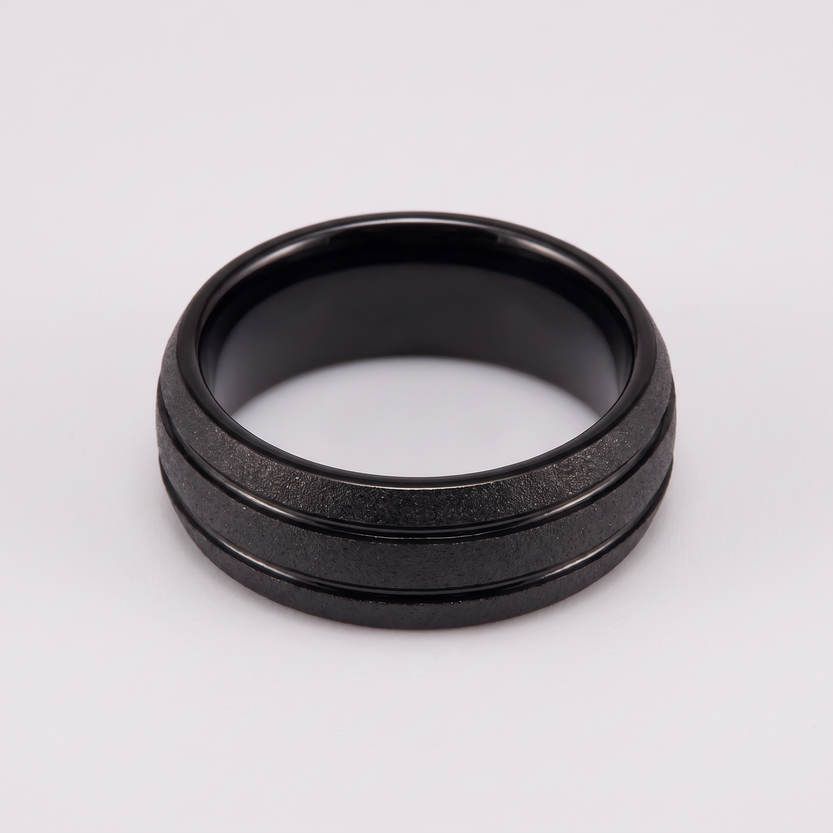 The Granite black sandblasted tungsten ring lying flat on a light grey surface