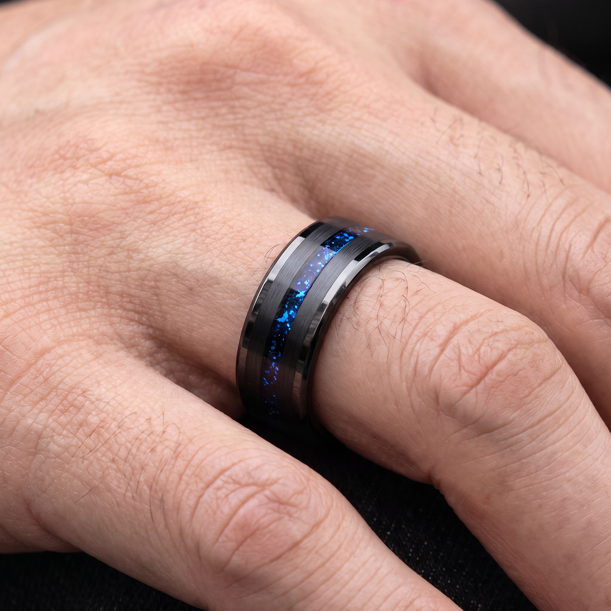 Man's hand wearing the black tungsten ring with blue galaxy inlay