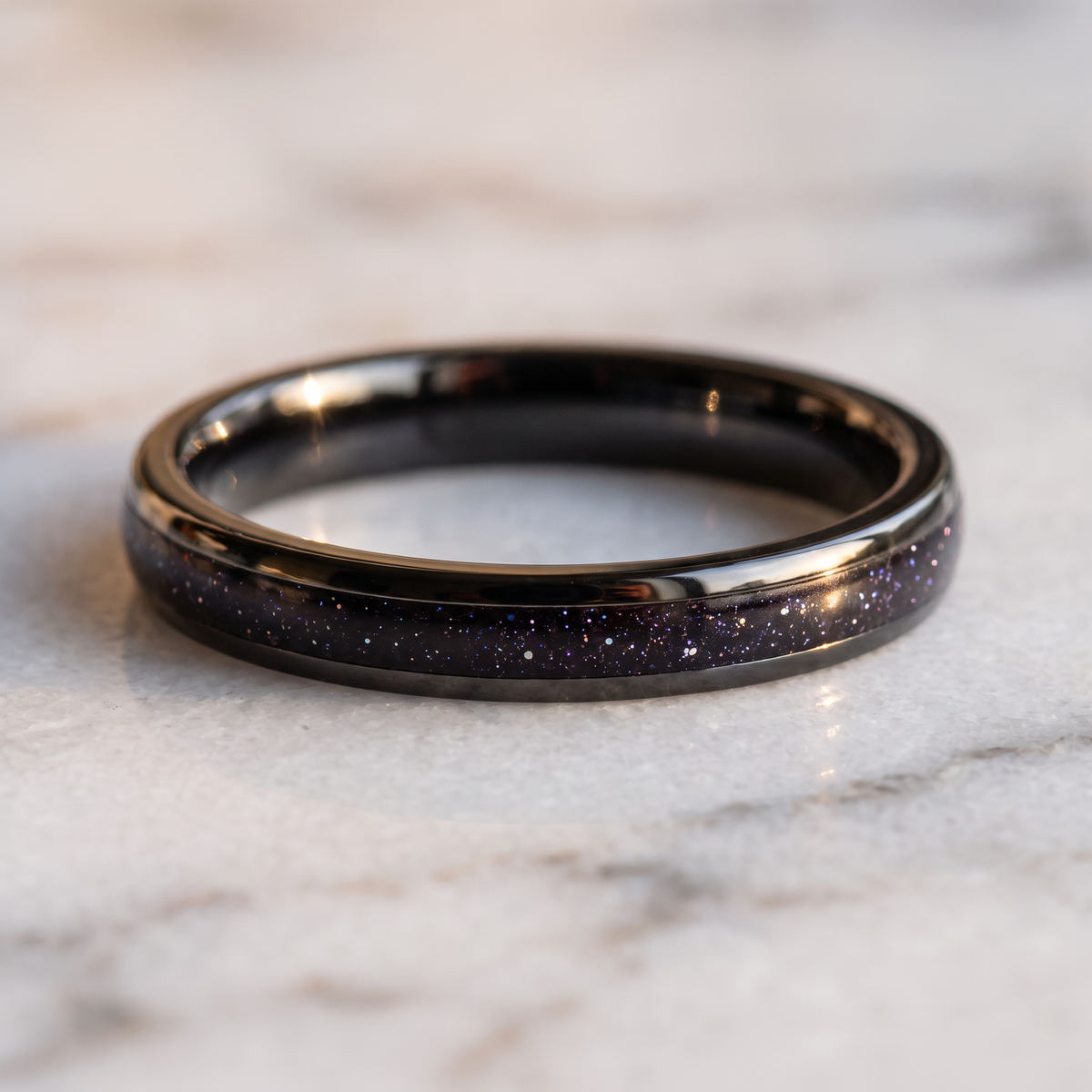 The Vega black tungsten ring with a galaxy opal inlay lying flat on a marble surface