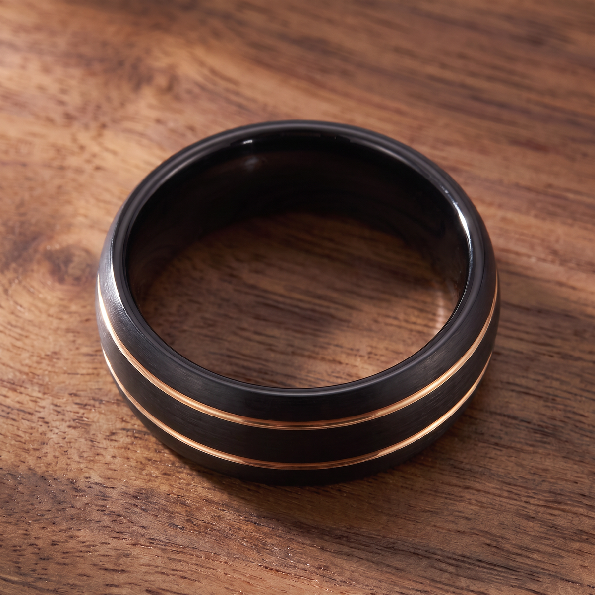 The Riptide black tungsten ring with a double gold line inlay lying flat on dark walnut wood