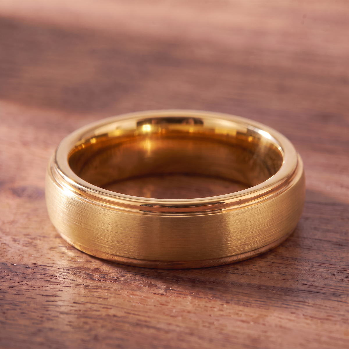 The Corona gold color tungsten ring lying flat on dark walnut wood