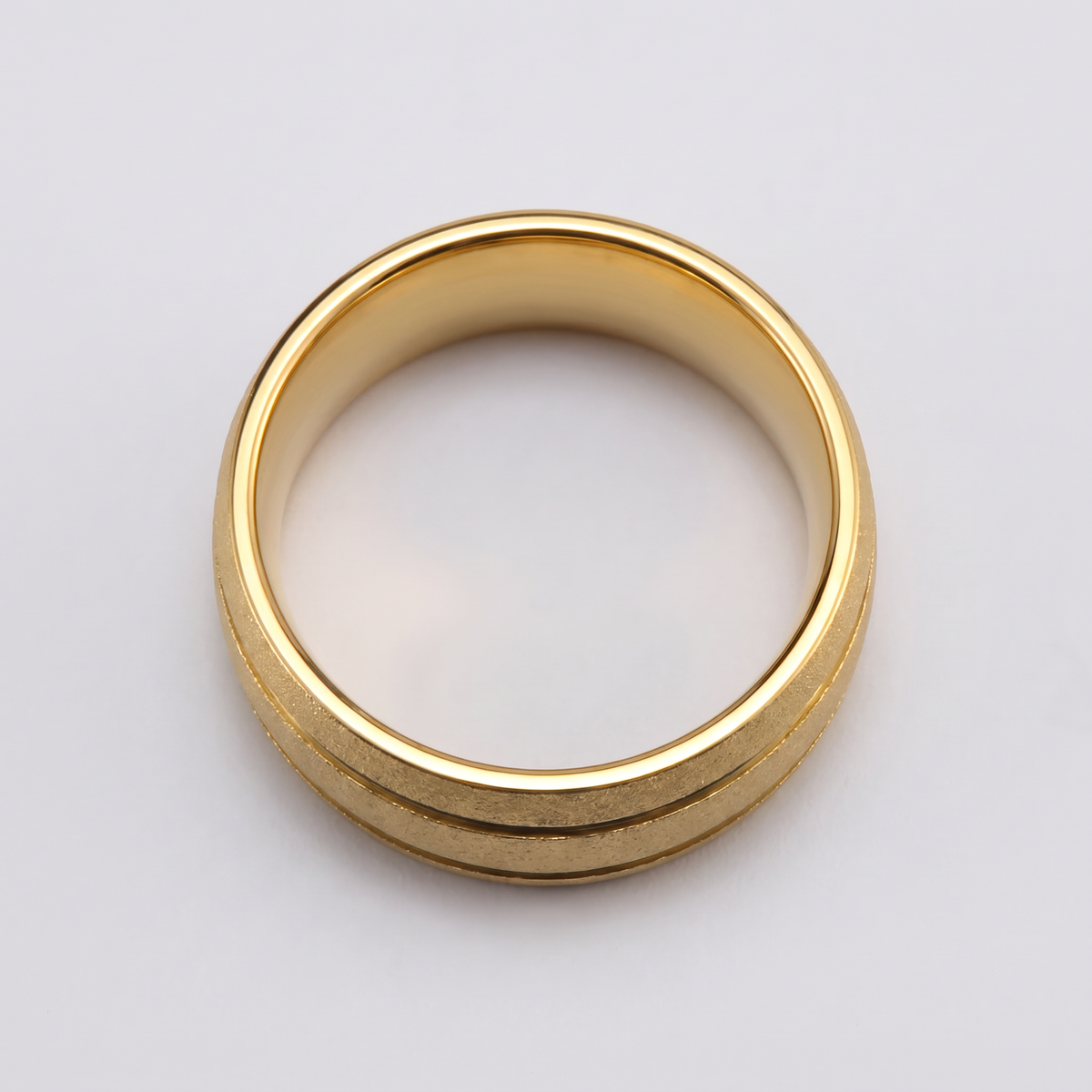 The Granite gold sandblasted tungsten ring lying flat on a light grey surface