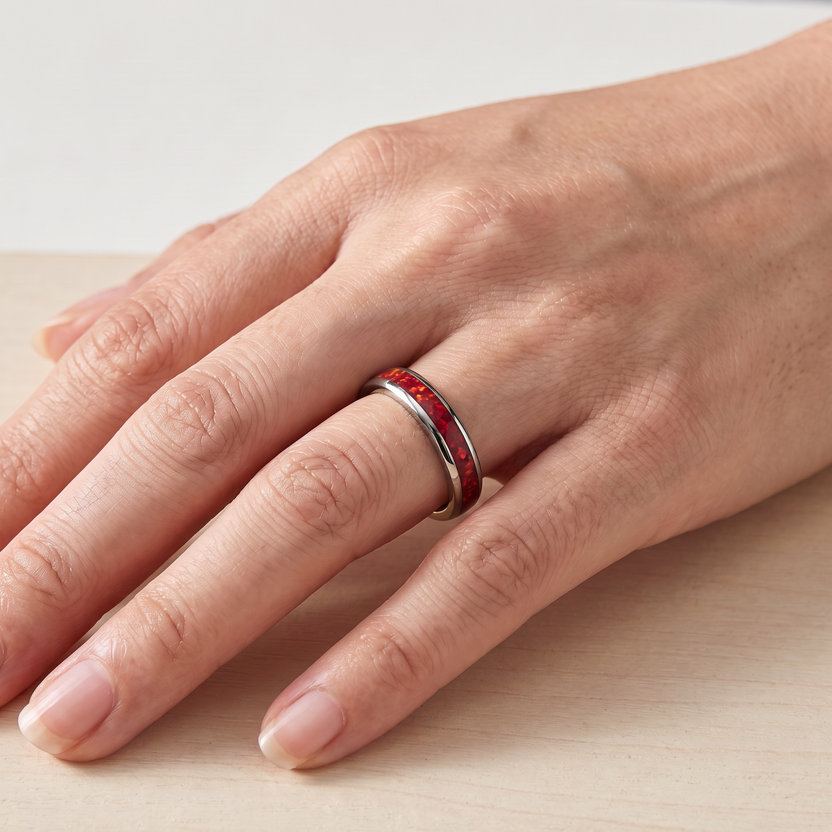 Close up of a woman's hand wearing The Cinder silver color tungsten ring with a red opal inlay