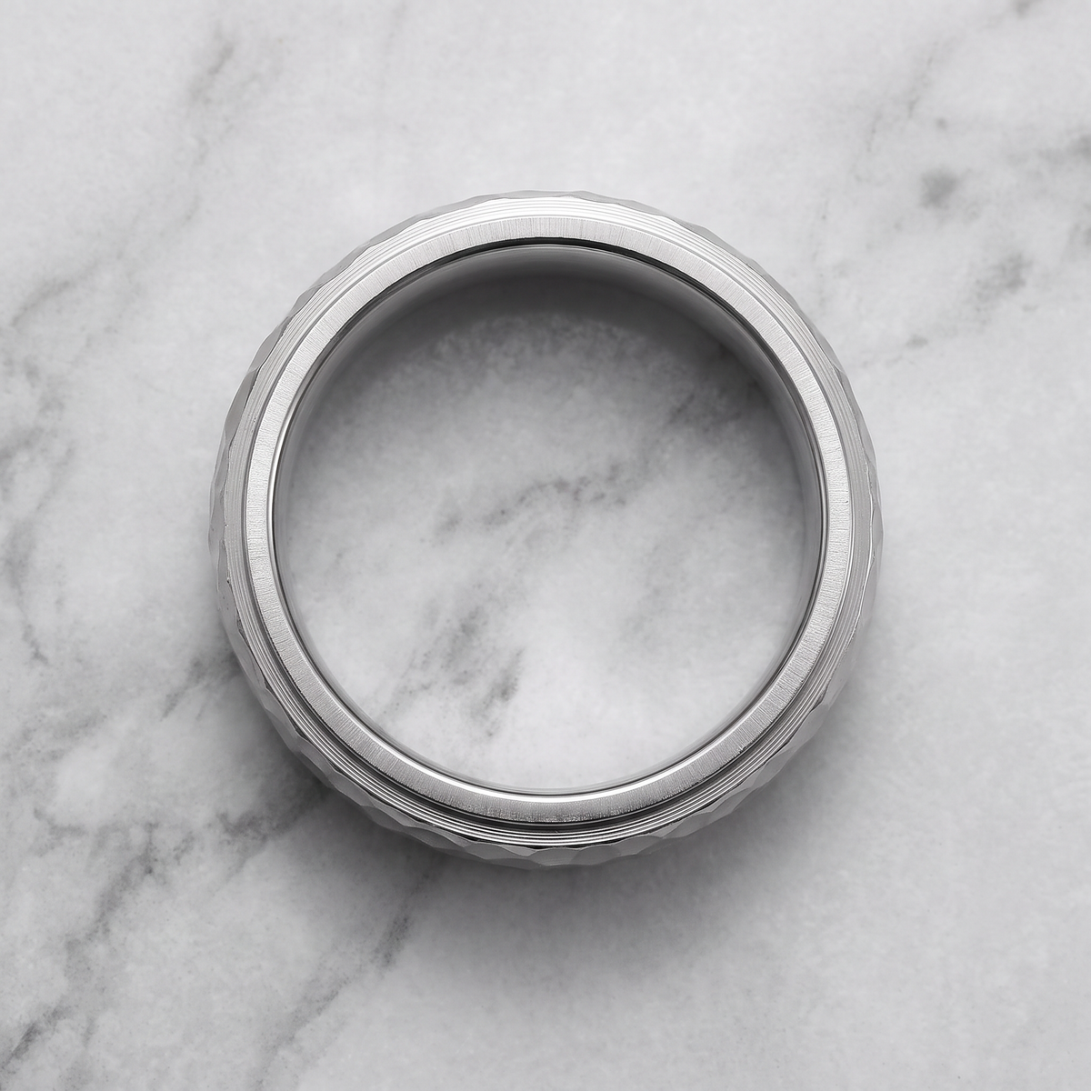 The Crater silver hammered ring lying flat on a light grey marble surface