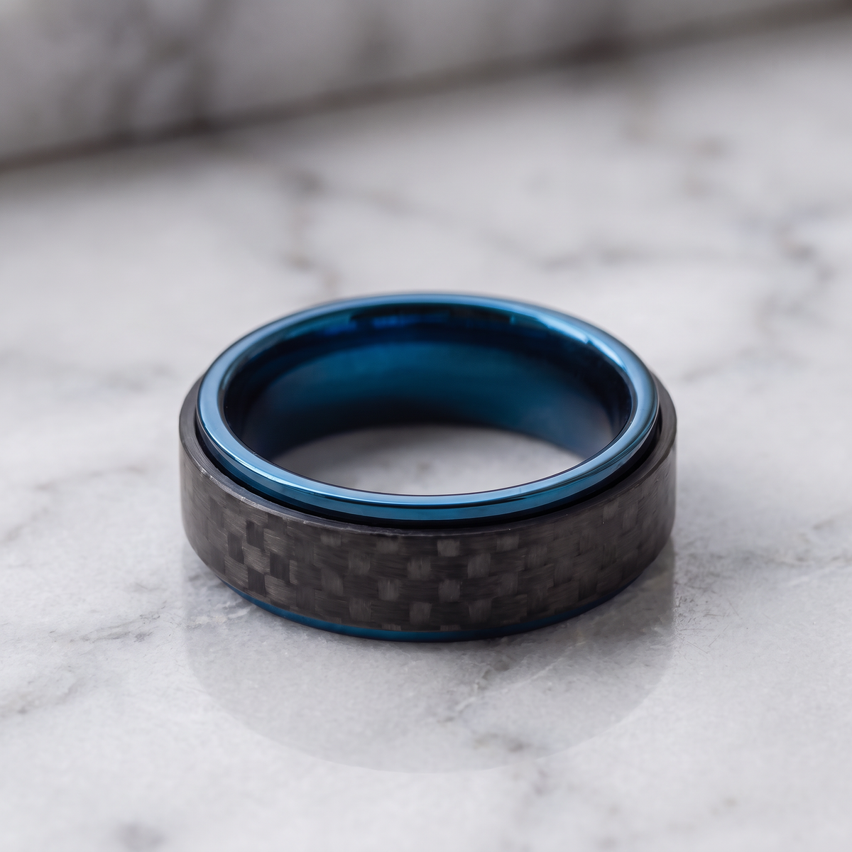 The Spinner carbon fiber ring lying flat on a light grey marble surface