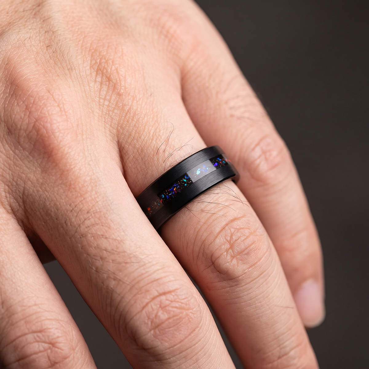 Man's hand wearing the black tungsten ring with opal inlay
