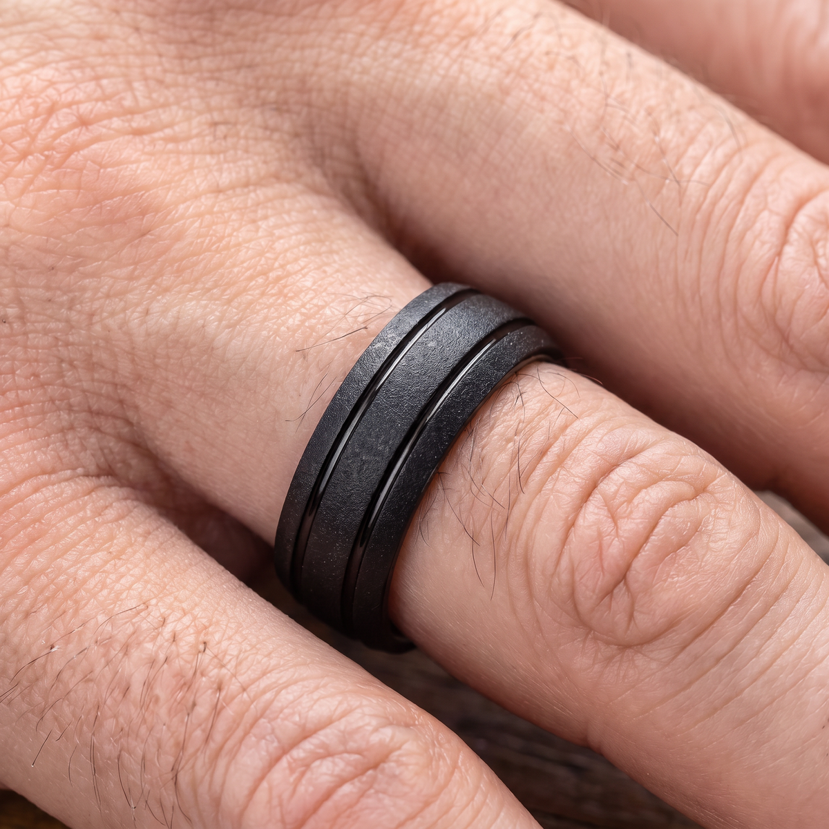 Close up of a man's hand wearing The Granite black sandblasted tungsten ring