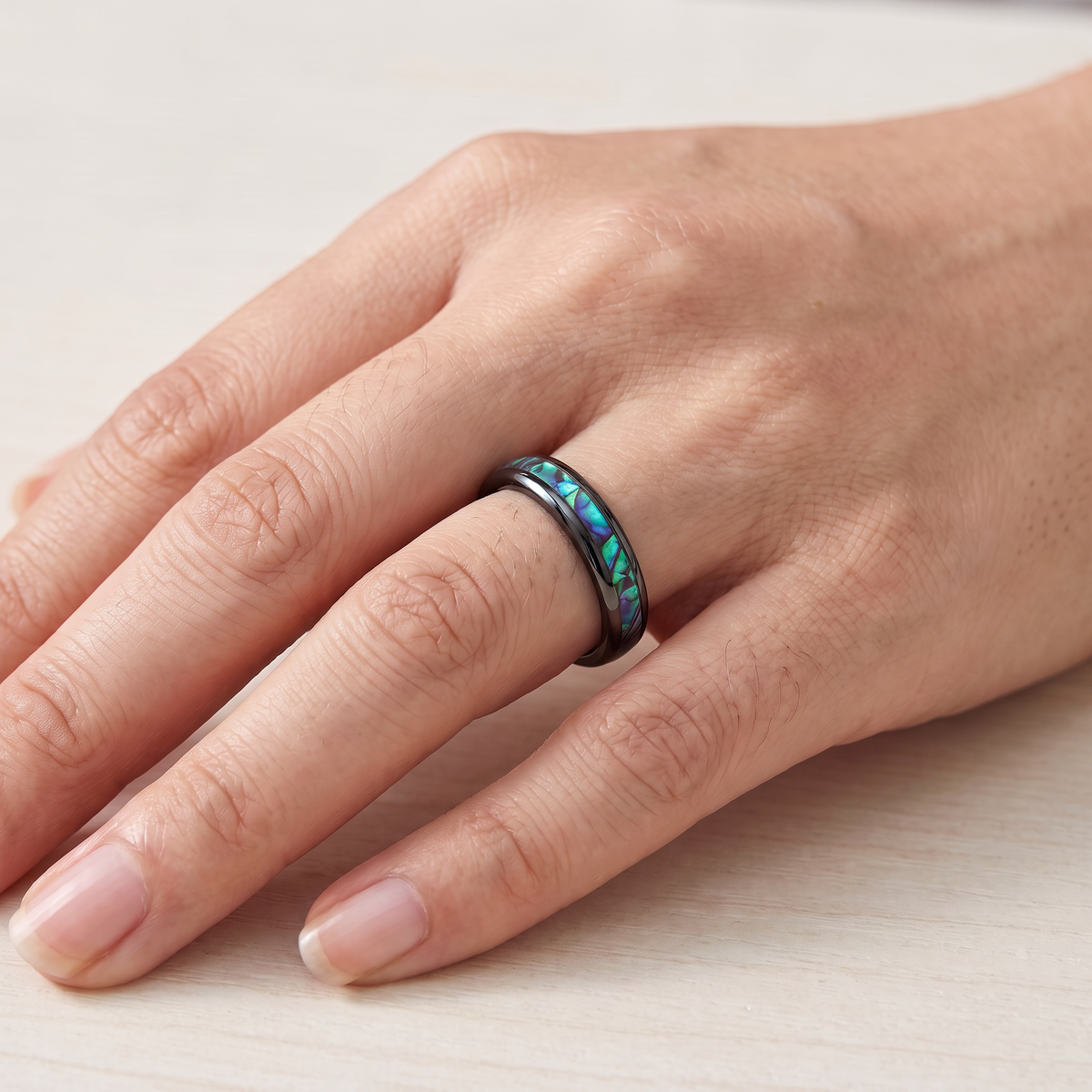 Close up of a woman's hand wearing The Iris black tungsten ring with an abalone shell inlay