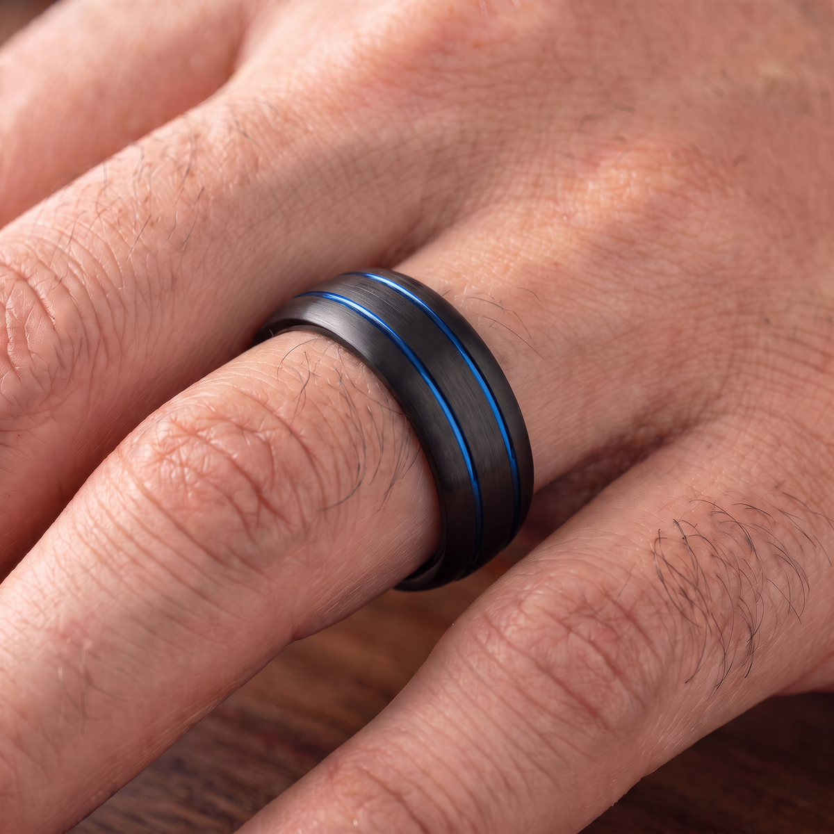 Close up of a man's hand wearing The Riptide black tungsten ring with a double blue line inlay