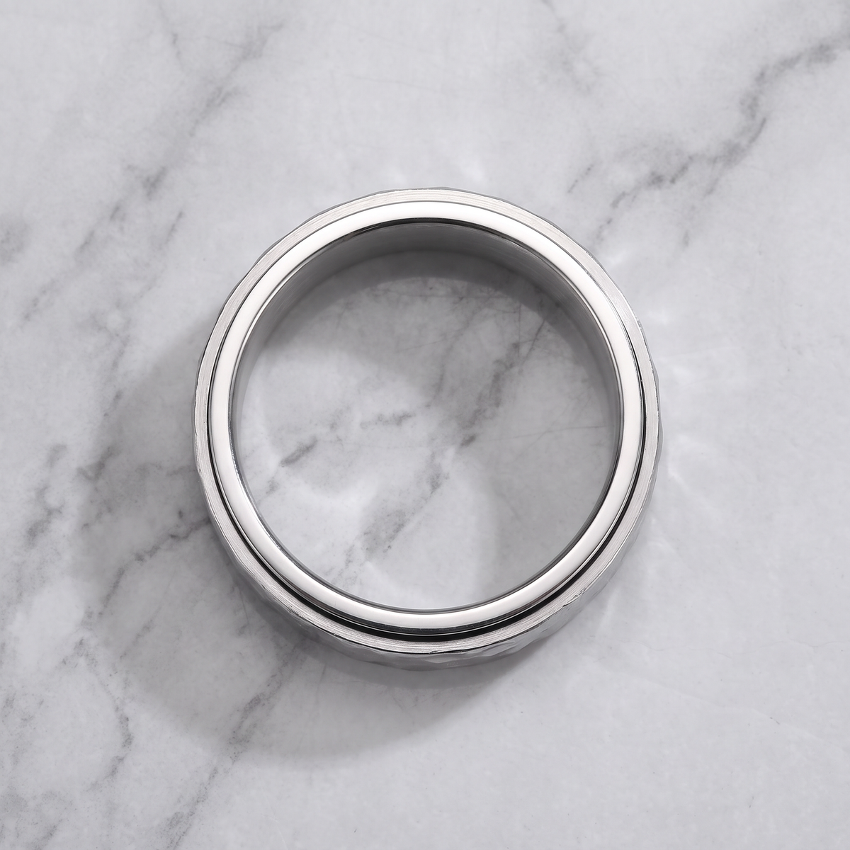 The Orbit silver spinner ring lying flat on a light grey marble surface
