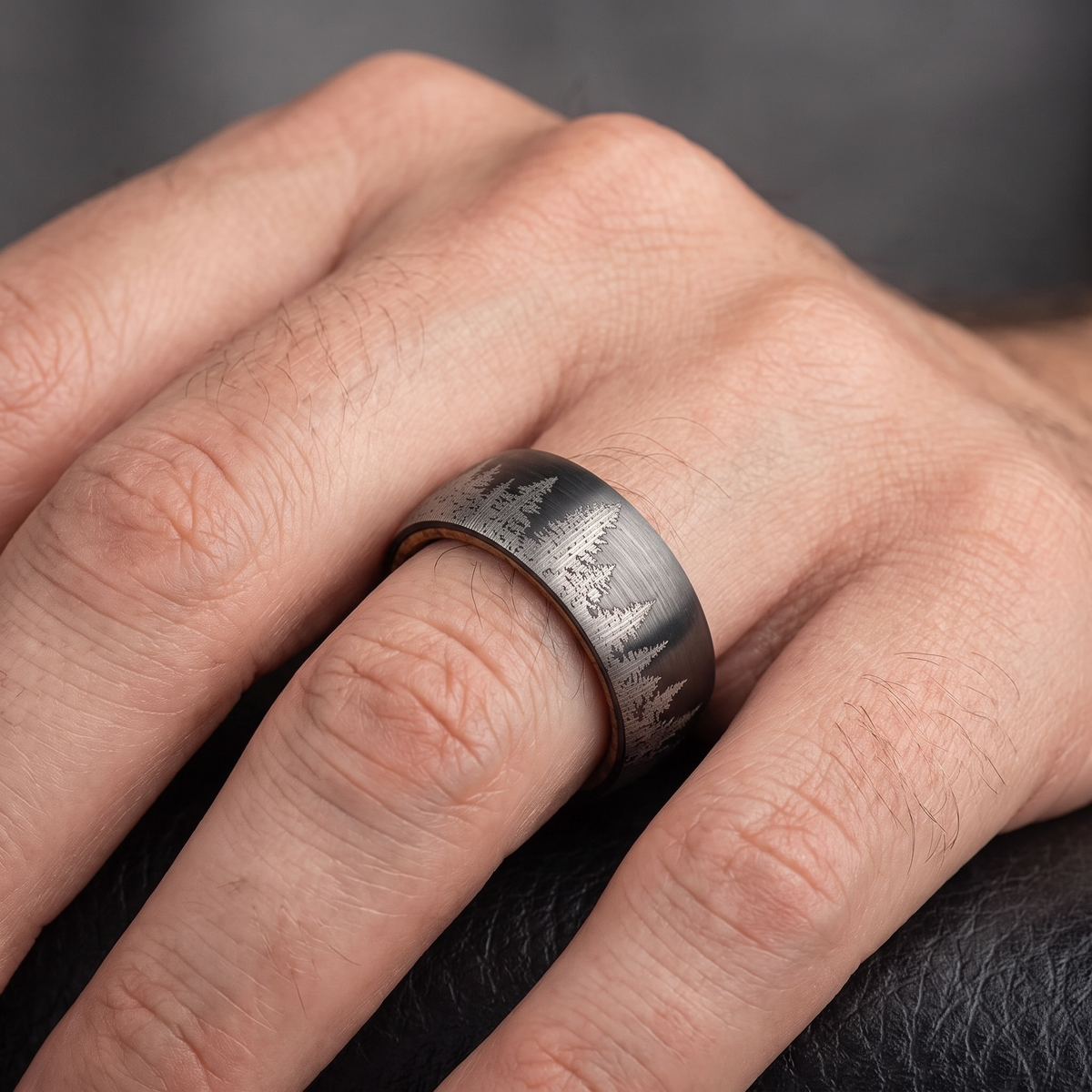 Man's hand wearing The Timberline brushed tungsten ring with forest pattern