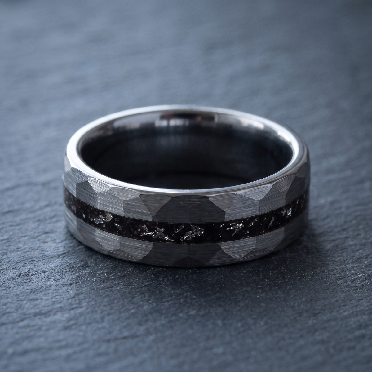 The Meteor hammered tungsten ring lying flat on a dark slate stone surface