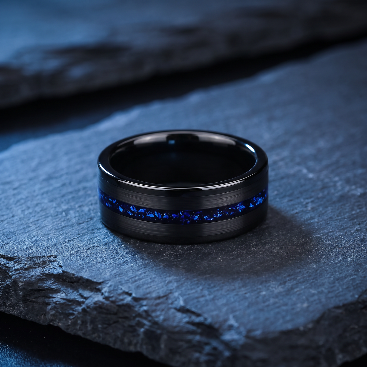 Black brushed tungsten ring with blue galaxy inlay lying flat on dark slate