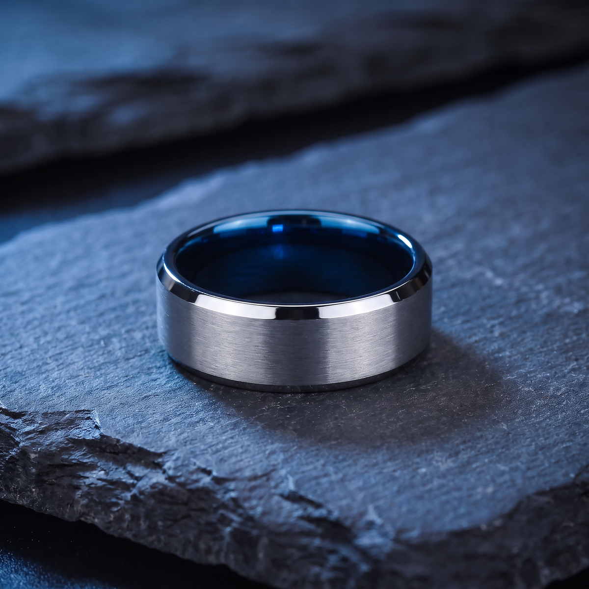 The Fathom 8mm silver tungsten ring with a blue inside lying flat on dark slate