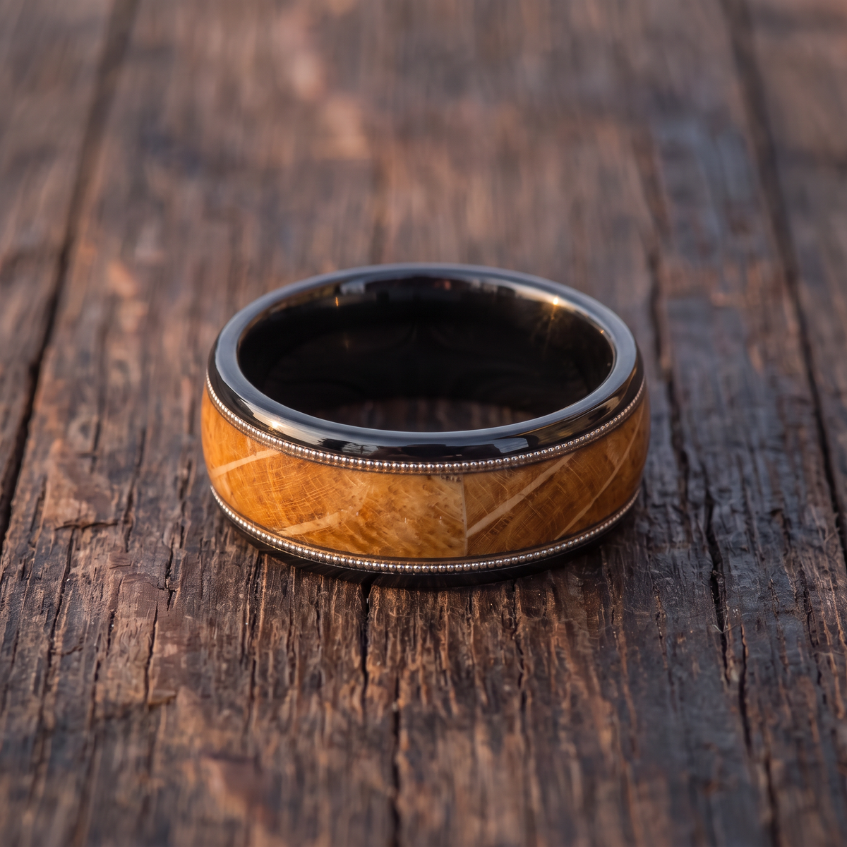 The Encore black tungsten ring with barrel wood inlay lying flat on weathered dark oak
