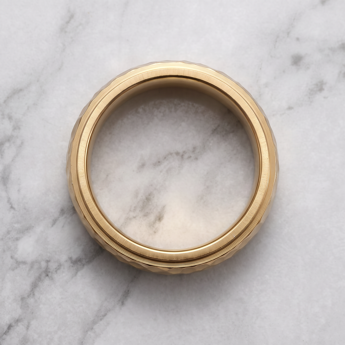 The Crater gold hammered ring lying flat on a light grey marble surface