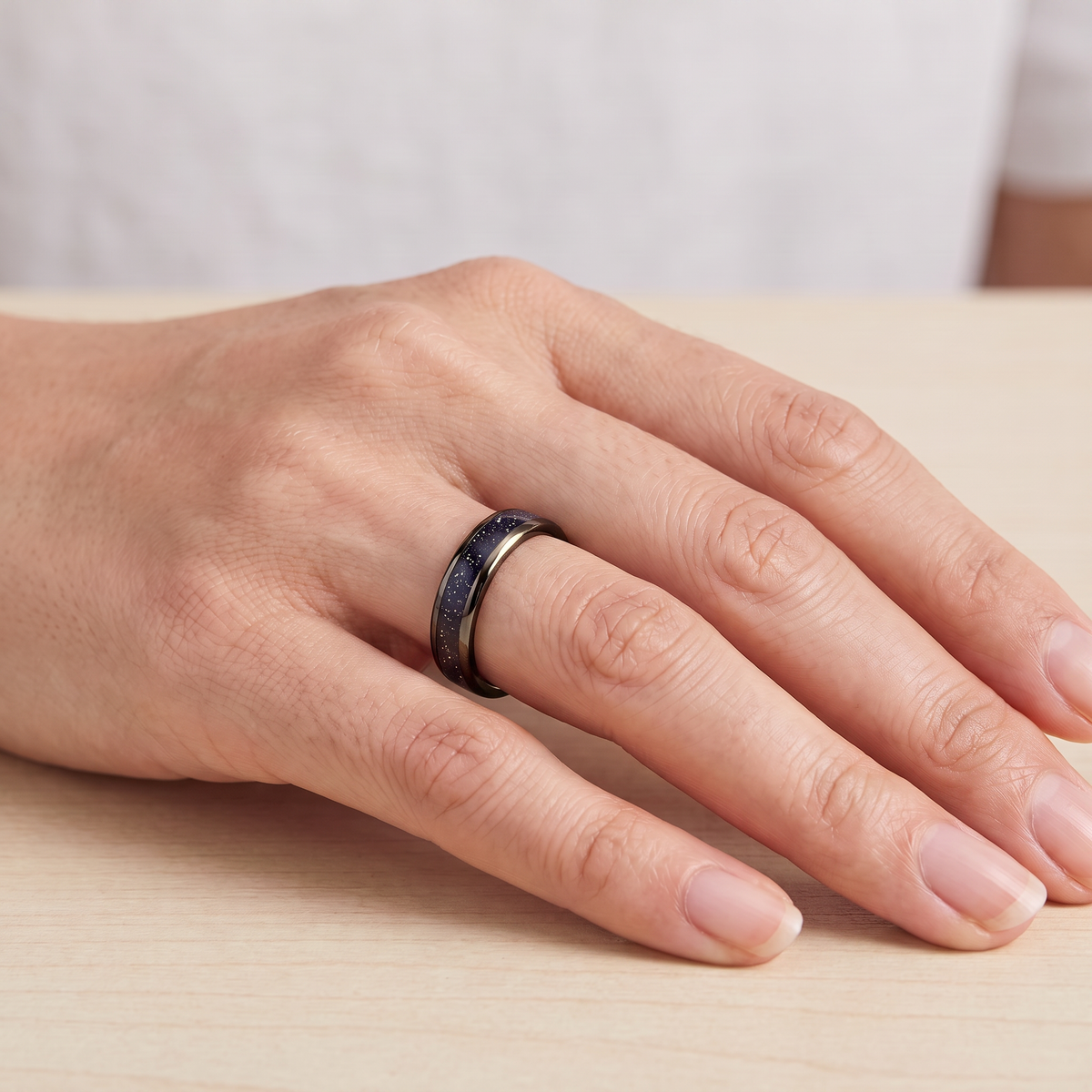 Close up of a woman's hand wearing The Vega black tungsten ring with a galaxy opal inlay